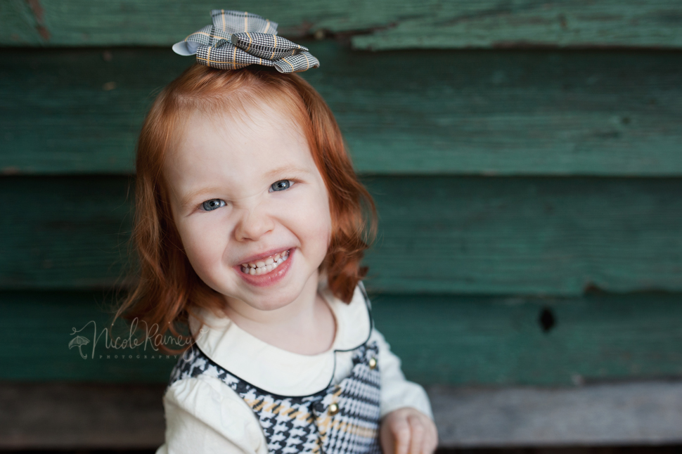 Smiling red headed little girl by green wall